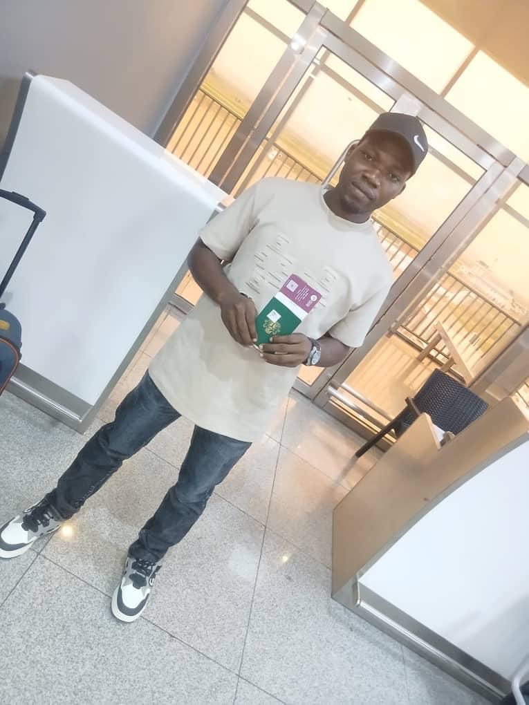 A candidate in a cap holding his passport near the terminal gate doors